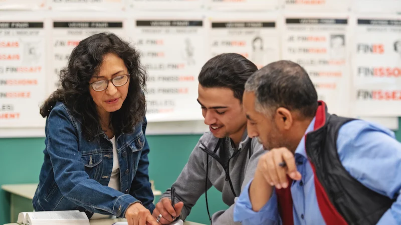 2 adults students speaking with their teacher while they are talking notes