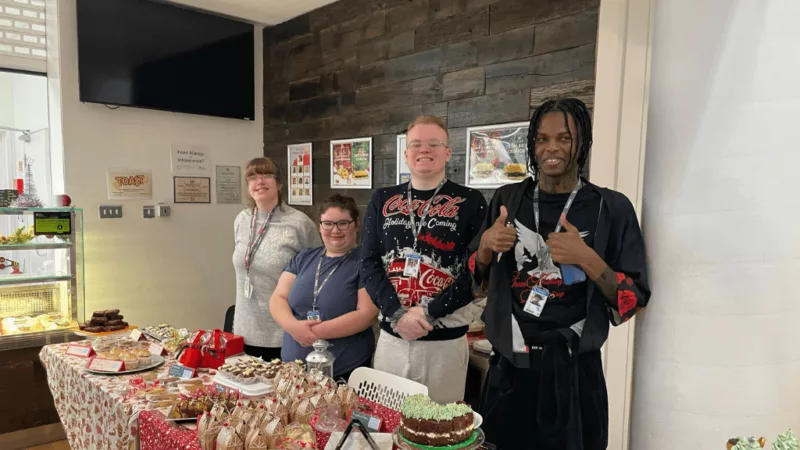 A group of people posing at a bakery event with cakes and festive treats.